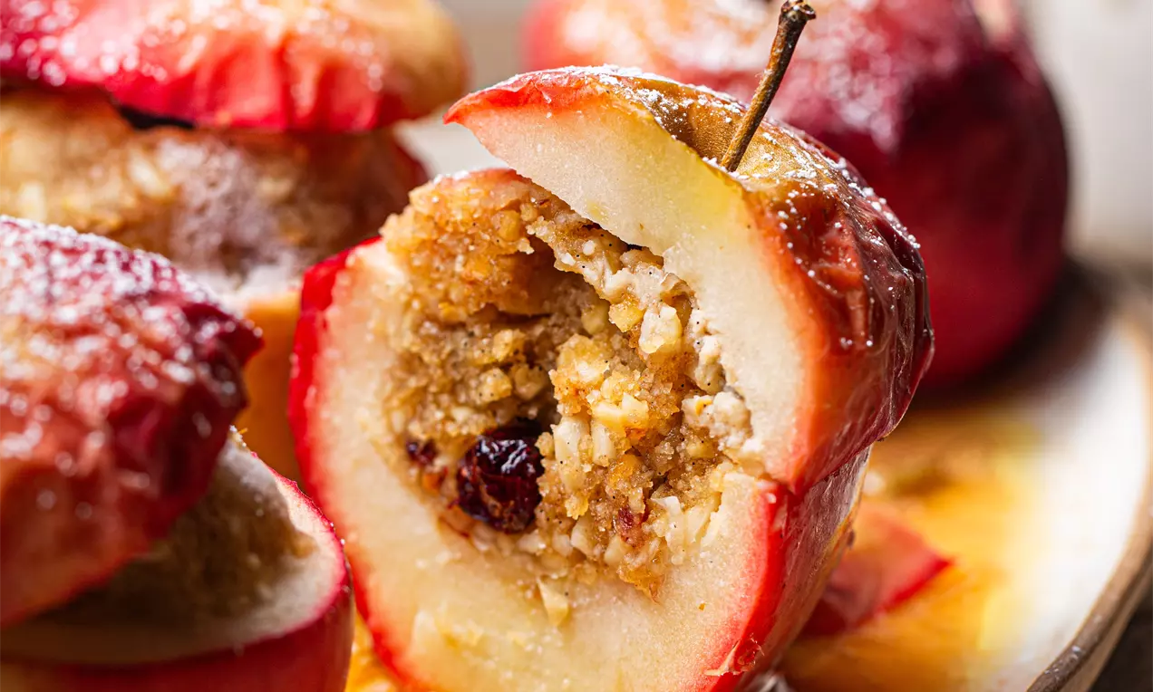 Picture - Baked red apples with glossy caramel glaze, hollowed and filled with crumbly nut mixture and raisins, served on a warm-toned plate