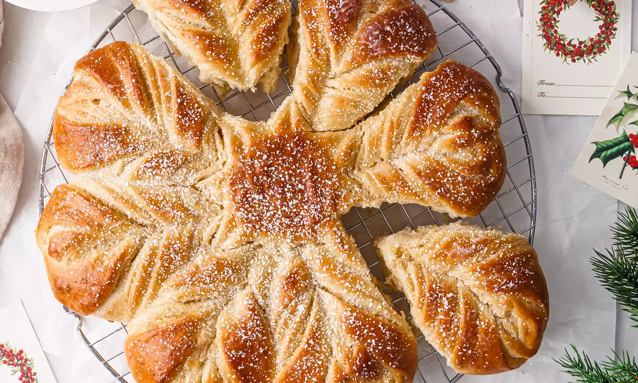 Picture - Golden vanilla star bread with twisted layers, dusted with sugar and arranged on a cooling rack, surrounded by festive details