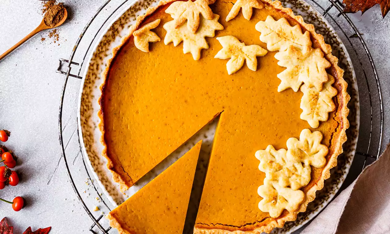 Picture - Golden vanilla pumpkin pie with smooth orange filling, a flaky crust, and leaf-shaped pastry decorations on a cooling rack